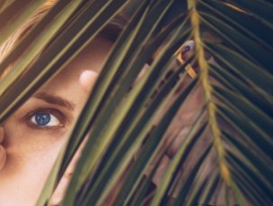 Beautiful blue-eyed woman looking through palm tree leaf